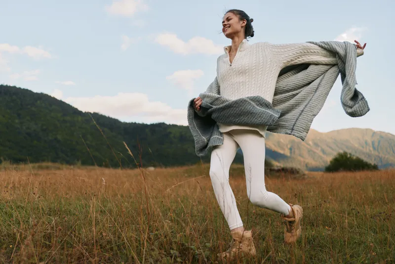 Joyful runner crosses a windy meadow in a cozy cardigan, feeling freedom and joy as the countryside opens up