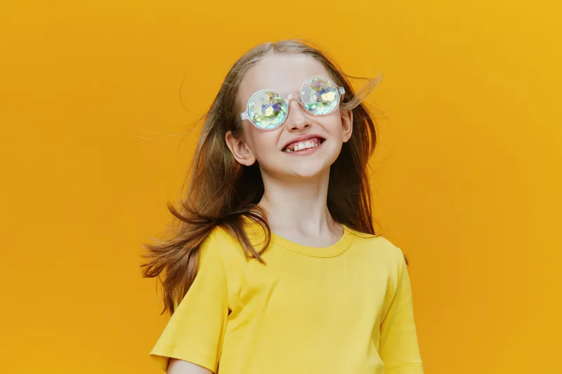 Cheerful young girl wearing stylish sunglasses and a yellow t shirt against a vibrant yellow background, embodying joy and summer vibes