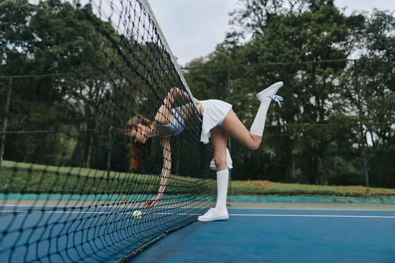 Young female tennis player in action, wearing a stylish white outfit, reaching for a tennis ball, showcasing determination and athleticism