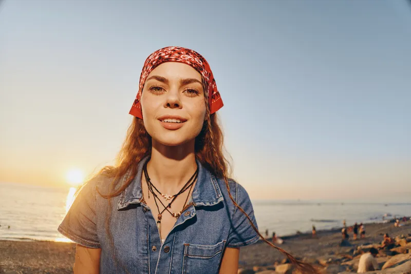 Lifestyle woman wearing modern boho-western denim street style outfit with a red bandana at sunset, film color effect highlighting warm natural light and relaxed mood.