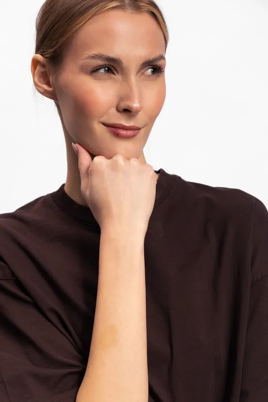 Thoughtful young woman with light skin and blonde hair looks sideways while resting her chin on her hand. Clean white background emphasizes calm and introspective mood.