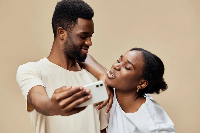 Happy young African couple taking a selfie together against a beige background, showcasing love, joy, and connection in a candid moment