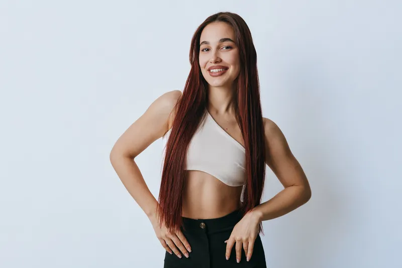 Young woman with long braids smiling and posing with hands on hips against white background. Casual style, confident expression and natural look in studio portrait.