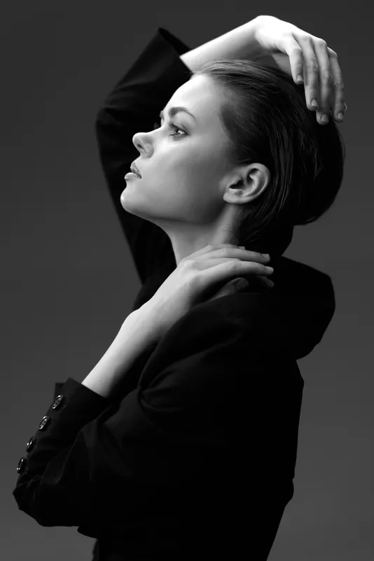 Black and white portrait of a stylish woman with slicked-back hair posing confidently in a dark outfit
