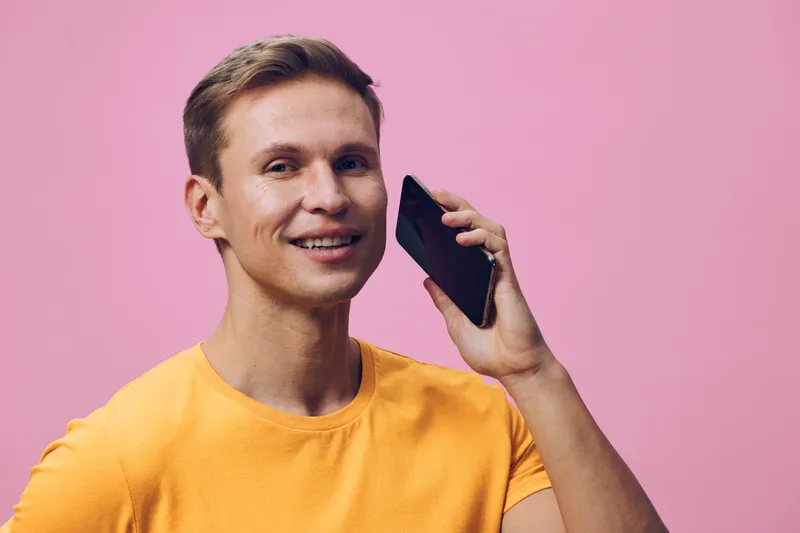 smiling young man wearing orange t-shirt talking on phone isolated on pink background digital nomad concept communication technology