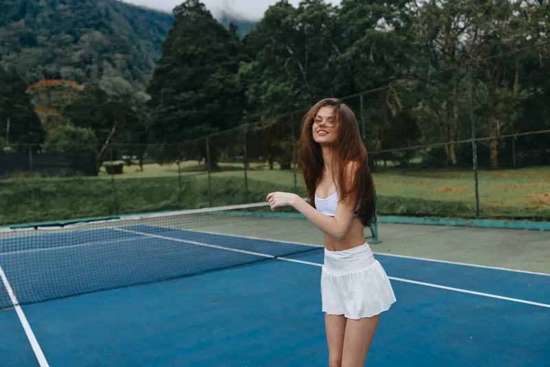 Young female tennis player enjoying a sunny day on the court, wearing a white sports outfit, exuding joy and confidence in a vibrant green outdoor setting