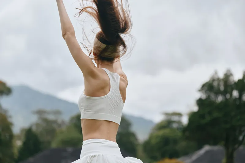 Graceful woman dancing outdoors, showcasing joy with flowing hair, minimalist clothing, and natural surroundings in a vibrant, seasonal landscape