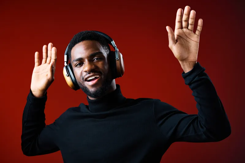 Stylish young African American man wearing headphones, dancing joyfully against a vibrant red background, conveying music and happiness