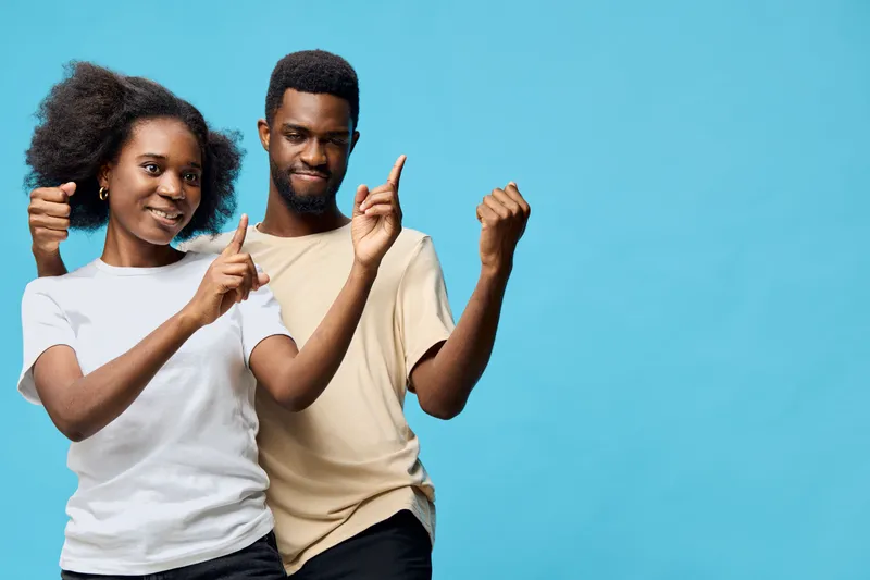Joyful young Black couple dancing against a vibrant blue background, expressing happiness and connection Stylish casual clothes enhance their fun vibe