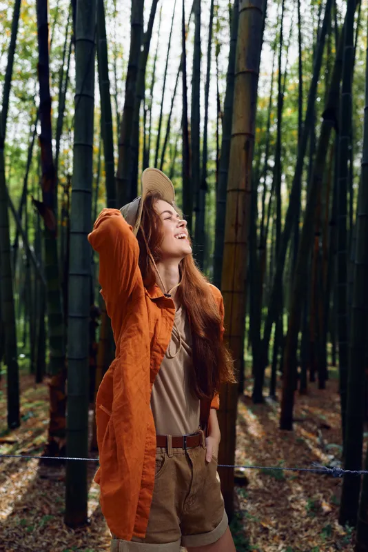 Woman bamboo forest nature portrait with hat and casual outfit, smile and straw hat as she enjoys travel outdoors among tall green trunks and serene woodland atmosphere.