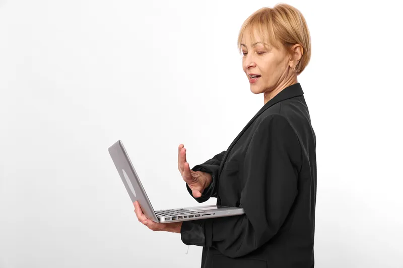 Woman with laptop in business attire, technology communication concept, professional profile on white background, speaking while holding keyboard, copy space, studio lighting.