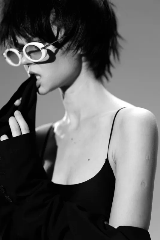 Black and white portrait of a stylish woman wearing round sunglasses, expressing thoughtful mood and modern fashion.