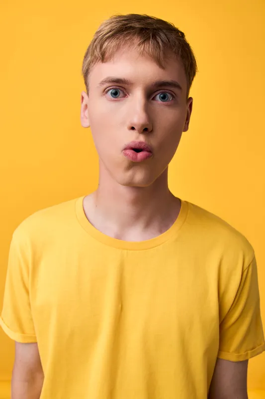 Surprised young man in a bright yellow shirt against a vivid yellow backdrop, wide eyes and puckered lips conveying playful astonishment with bold color, studio lighting and soft shadows for