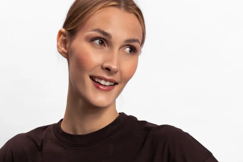 Smiling young woman with blonde hair looks to the side wearing a dark sweater. Studio portrait on white background. Concept of happiness, youth, beauty, and casual fashion.