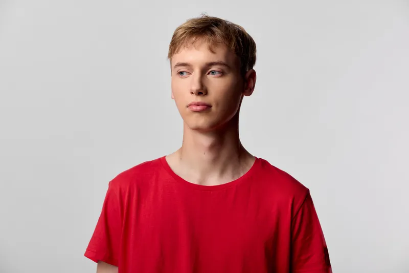 Young man in a red tee poses against a neutral backdrop with a thoughtful expression, studio lighting highlights clean lines, casual fashion style for versatile lifestyle stock use
