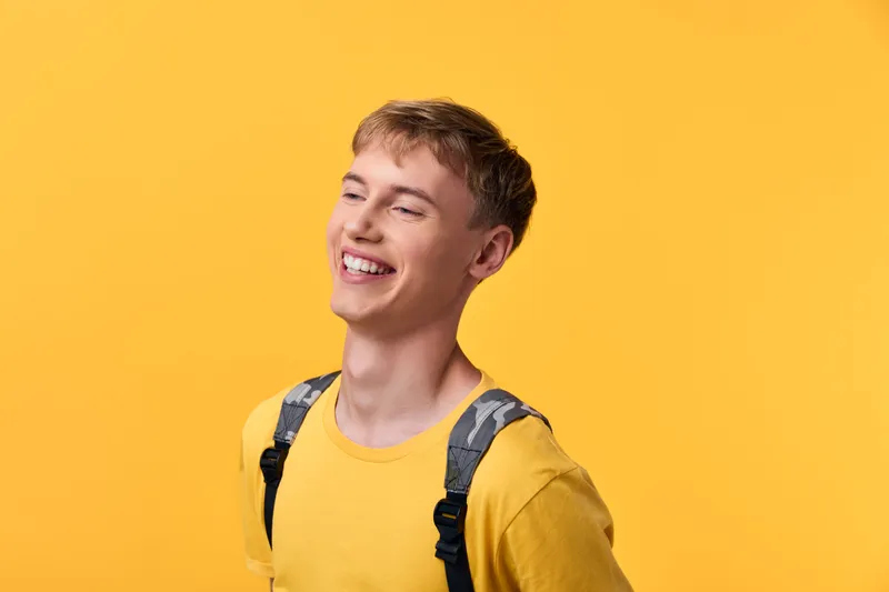 Young man wearing a yellow shirt and backpack, smiling against a bright yellow background, conveying optimism, energy, and casual everyday style