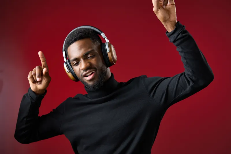 Young Black man enjoying music with headphones, dancing joyfully against a red backdrop, conveying energy and creativity