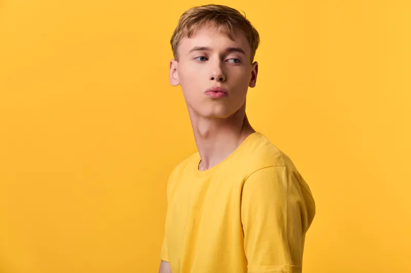 Young man in a yellow t shirt against a bright yellow backdrop, making a puckered kiss gesture for a playful fashion and lifestyle shot, vibrant color harmony and bold, cheerful mood