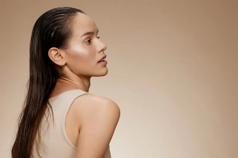 Young woman with sleek hair looking back, showcasing natural beauty against a soft beige background, ideal for beauty and hair care concepts
