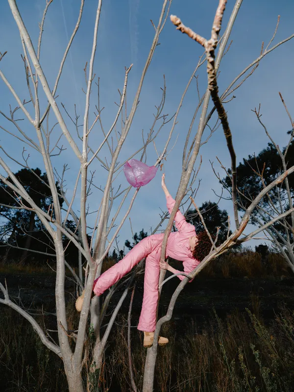 A child in pink clothing climbs a bare tree in an open field under a clear sky, capturing a playful moment of outdoor adventure and nature exploration and curiosity.