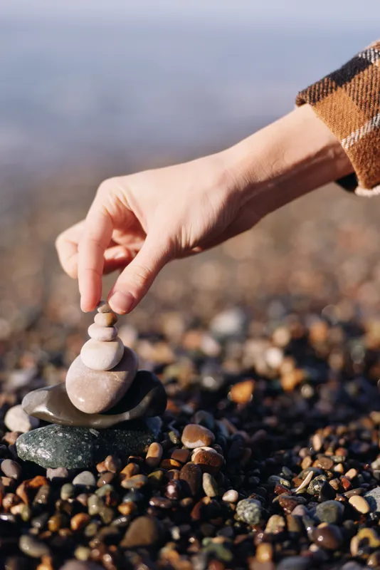Stone stacking on a pebble beach with a hand placing balanced rocks, capturing calm focus, mindfulness and a tranquil seaside moment in natural light and gentle textures.