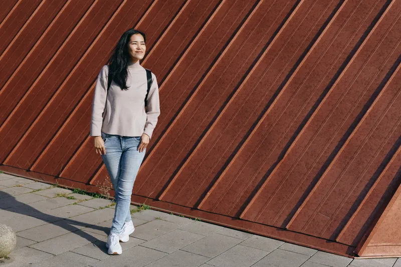 Woman standing street fashion casual outdoors urban wall diagonal backpack pose daylight lifestyle chic style casualwear everyday streetwear model outdoorsy sidewalk relaxed confidence and urban vibe
