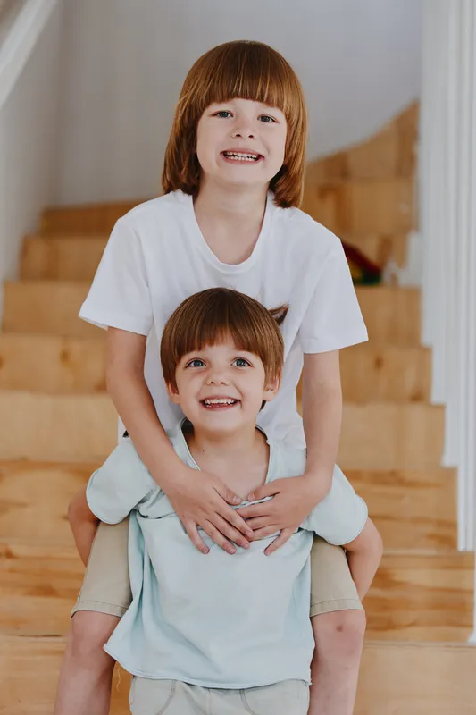 Two joyful boys smiling together while playing on the staircase, sharing a moment of happiness, capturing the innocence and warmth of childhood friendship.