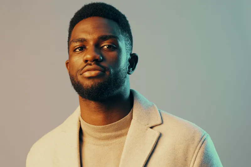 Confident young African man in stylish clothes posing against a soft green background, showcasing modern fashion and self assurance