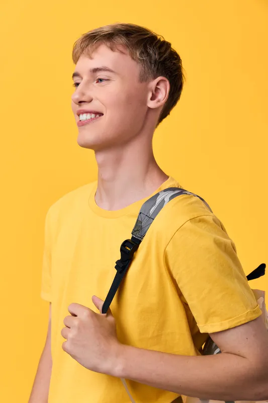 Student with yellow t shirt and backpack smiles against a bright yellow background, casual style and youthful energy, everyday life scene focusing on fashion, confidence, and cheerful mood for