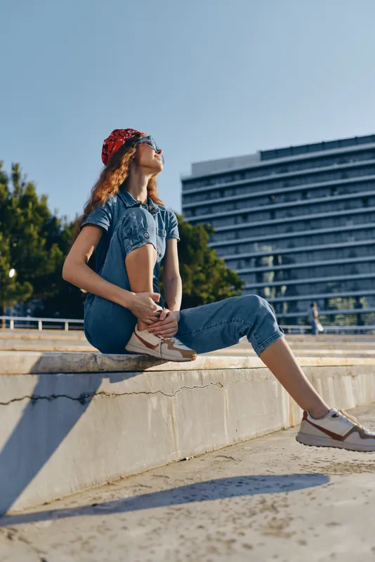 lifestyle woman in modern boho-western denim street style sitting outdoors with sunglasses and red bandana, capturing film color mood under bright sunlight