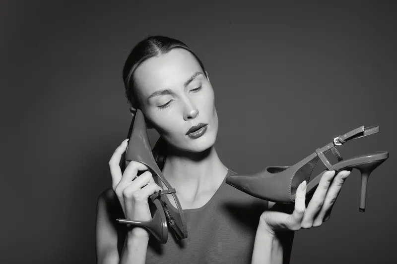 Caucasian woman with fair skin holds high heel shoes near her face with closed eyes, expressing calm and focus. Concept for fashion, footwear, and style.