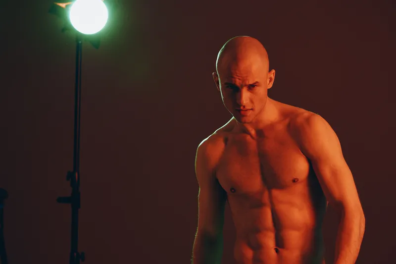 Muscular man posing confidently in dramatic lighting setup, showcasing strength and determination. The vibrant hues create a captivating visual impact.