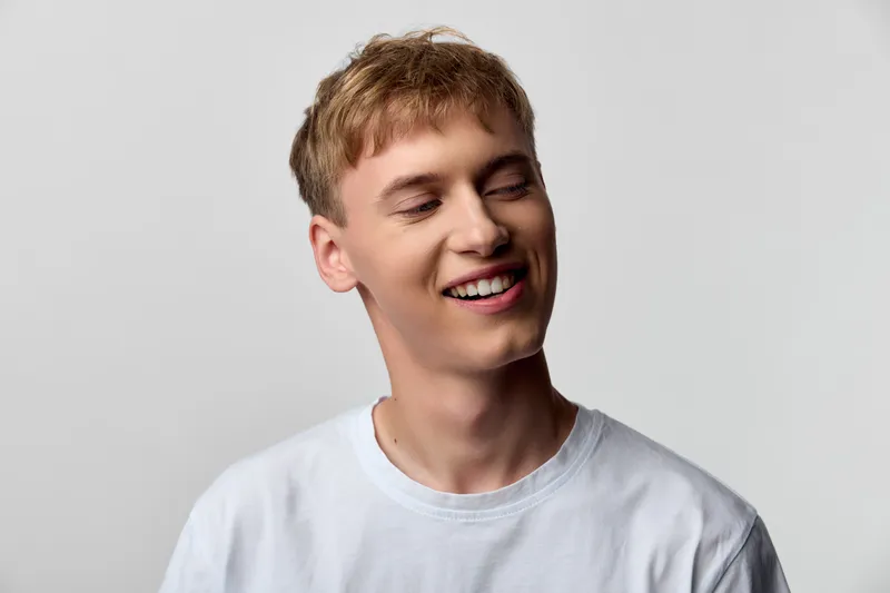 Smiling man in a white t shirt, head and shoulders shot with soft studio lighting, conveying casual happiness, relaxed mood and approachable vibe for lifestyle, fashion or advertising projects