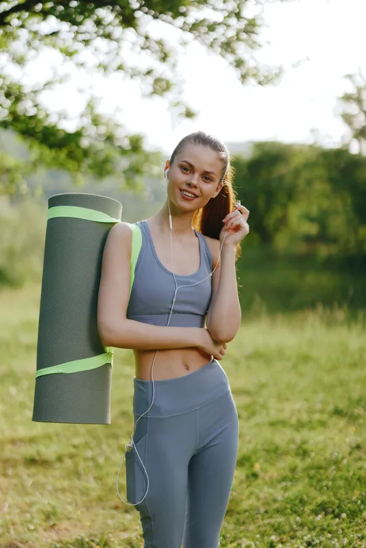 Young woman in athletic wear with yoga mat in nature, showcasing a positive attitude and health conscious lifestyle during summer outdoors