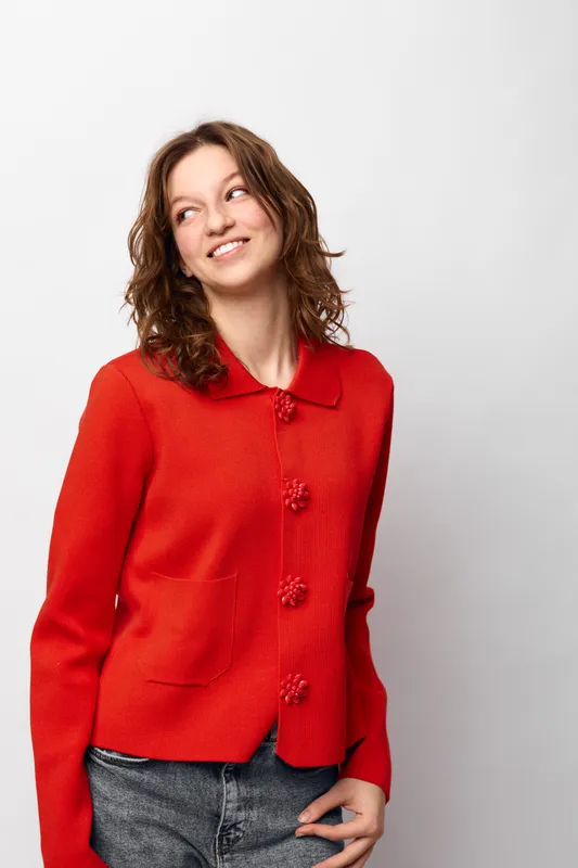 Young woman with curly brown hair wearing a red sweater and jeans looks sideways smiling. Casual style, positive mood, isolated on white background, studio portrait concept.