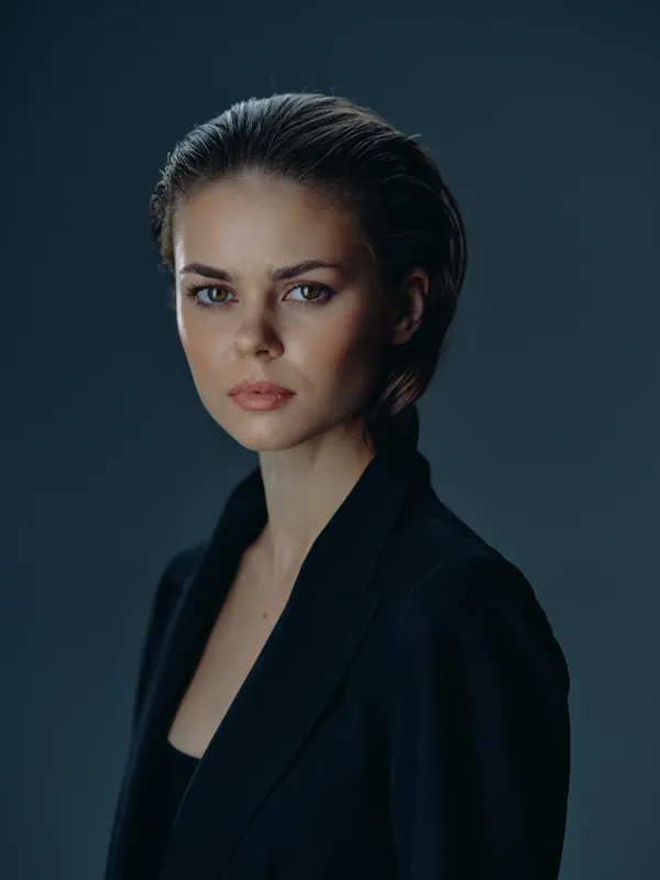 Serious woman with short hair wearing black suit against dark background, expressing confidence and professionalism.