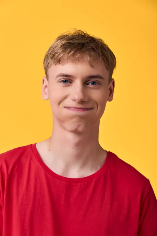 A young man with a friendly smile wearing a red shirt stands against a bright yellow background, conveying warmth, approachability, and casual style suitable for lifestyle and marketing campaigns.