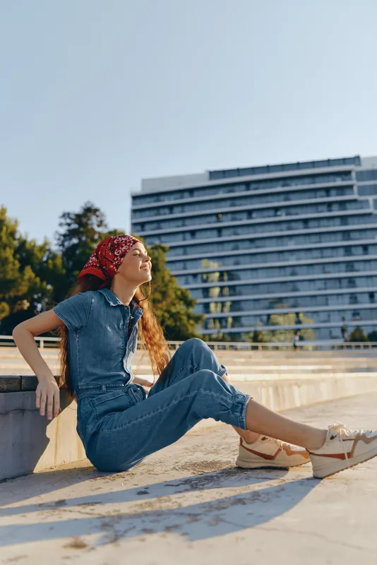 Lifestyle woman in modern boho-western denim street style wearing a red bandana, relaxed outdoors in film color with natural sunlight and urban background.