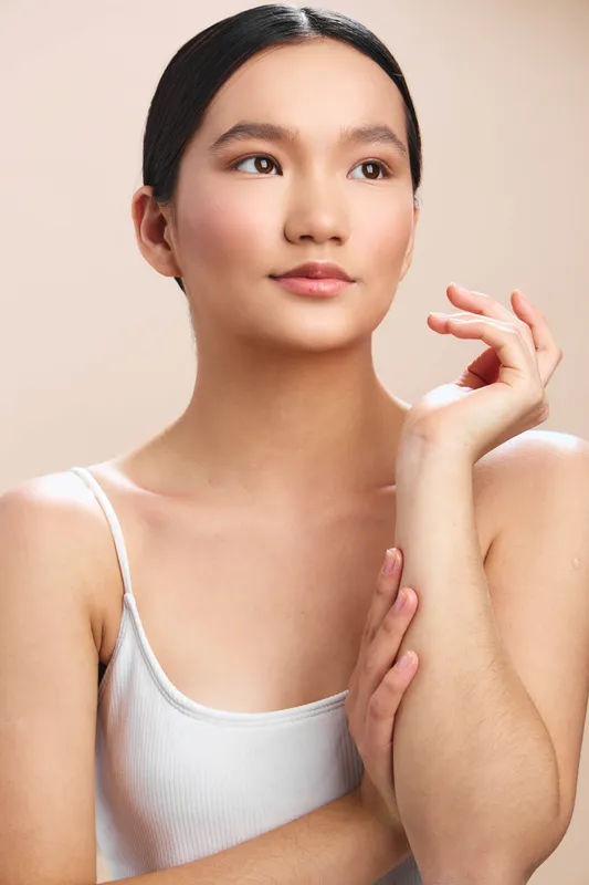 asian woman with smooth complexion gazes softly into distance, showcasing calm elegance in a studio portrait with warm lighting, minimal styling, and a serene mood, and gentle expression.
