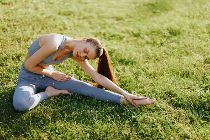 Young woman practicing yoga outdoors in a serene green field, demonstrating flexibility in activewear, conveying calmness and focus, ideal for wellness themes