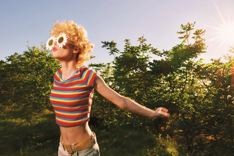 Bright woman with striped top and flower sunglasses runs through a sunlit park, embodying lively outdoor life. Retro colors create a joyful, playful mood and a sense of freedom.