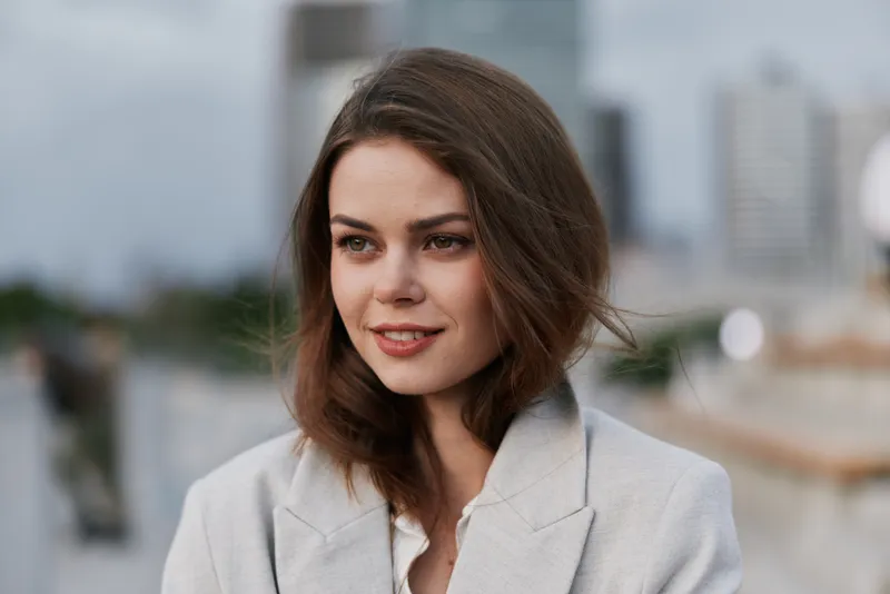 Businesswoman in a sophisticated suit with a confident smile, showcasing professionalism against a city skyline background.