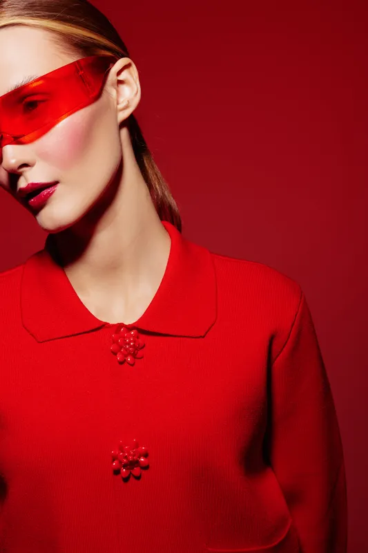 Stylish woman in red sweater and futuristic red sunglasses poses against red background. Fashion portrait with bold colors and modern accessories for editorial concept.