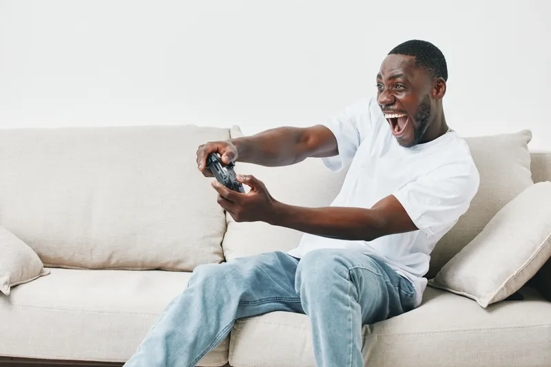 Excited young man playing video games on a couch, showcasing joy and enthusiasm in a cozy living room setting Bright colors enhance the vibrant atmosphere