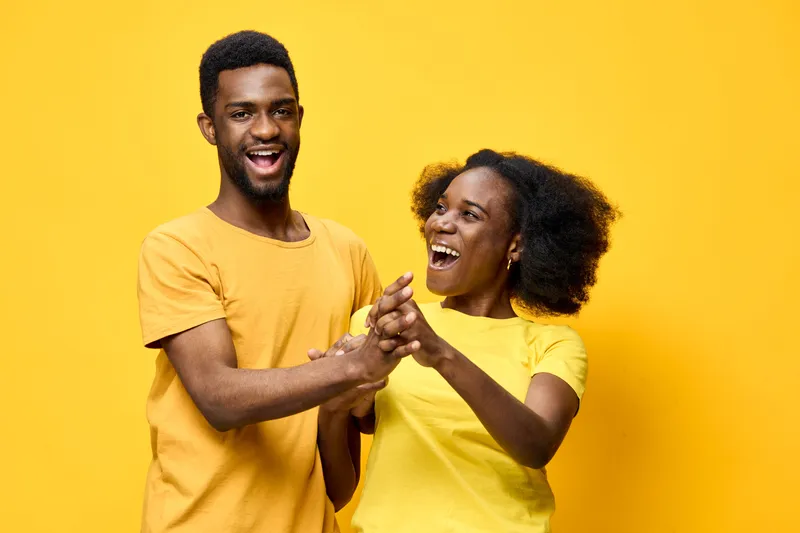 Happy young couple dancing together in vibrant yellow shirts against a bright yellow background, displaying joy and unity in a cheerful setting