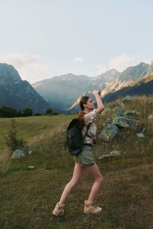 Cheerful woman hiking outdoors with a backpack in a mountain landscape, enjoying a sunlit moment among meadow and trail, conveying nature, travel and lifestyle in an adventurous mood
