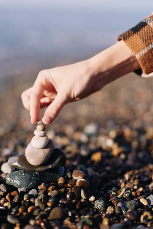 Balance, stones, hand, beach, pebbles, zen, mindfulness, harmony, stacking, meditation scene with a gentle hand placing stones on a rock tower by the shore