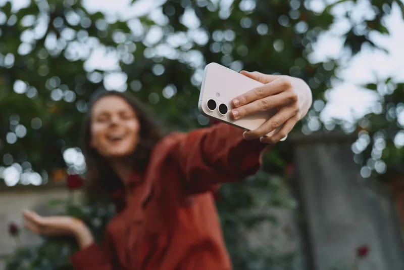 Cheerful woman outdoors taking a selfie, smiling with friends nearby, sunlit moment, casual outfit, warm tones, lens flare, natural colors, park backdrop, lifestyle shot