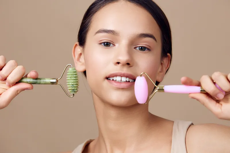 Young woman with facial rollers, showcasing beauty and wellness routine in a serene setting, emphasizing self care and natural skincare techniques