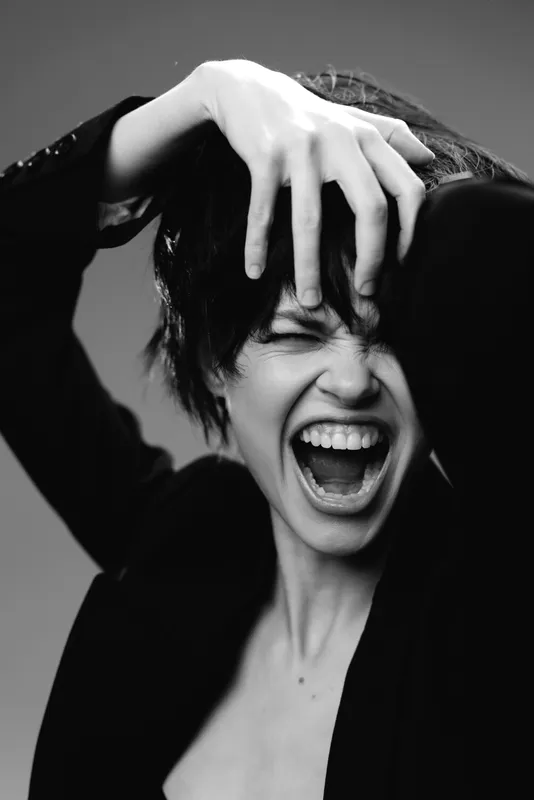 Black and white portrait of expressive woman shouting with hand in hair, conveying strong emotion and intensity.